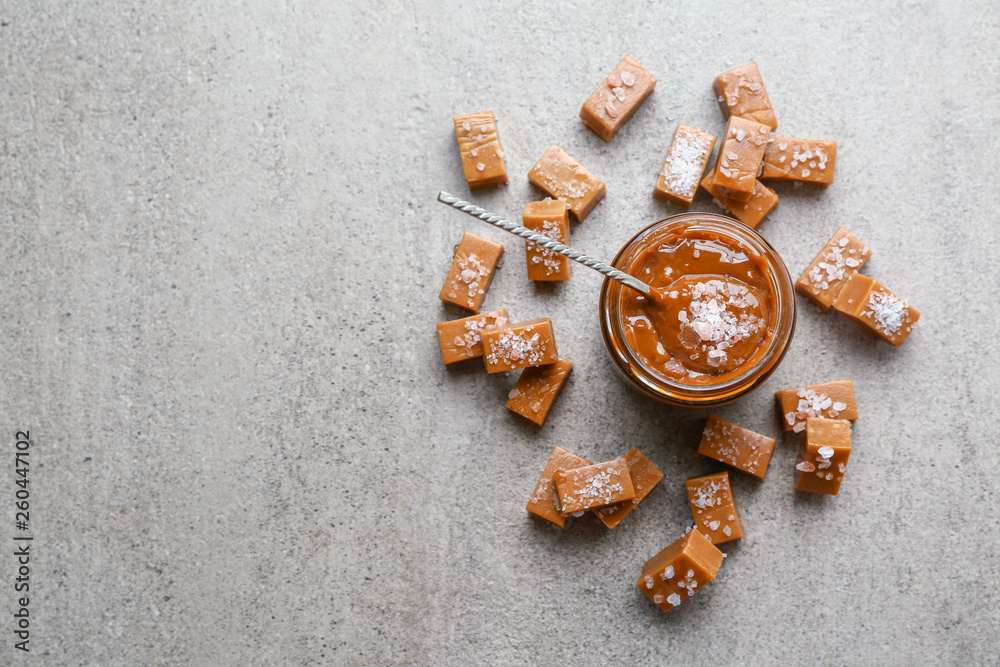 Jar of tasty salted caramel with candies on grey background