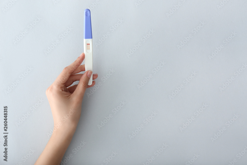 Female hand with pregnancy test on light background