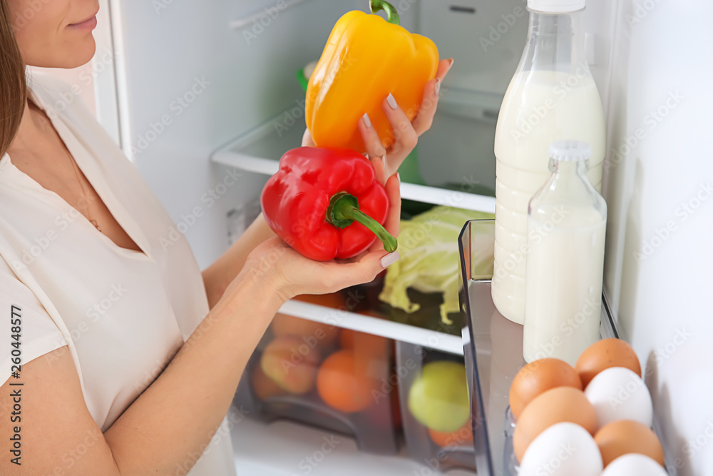 Woman taking pepper from fridge