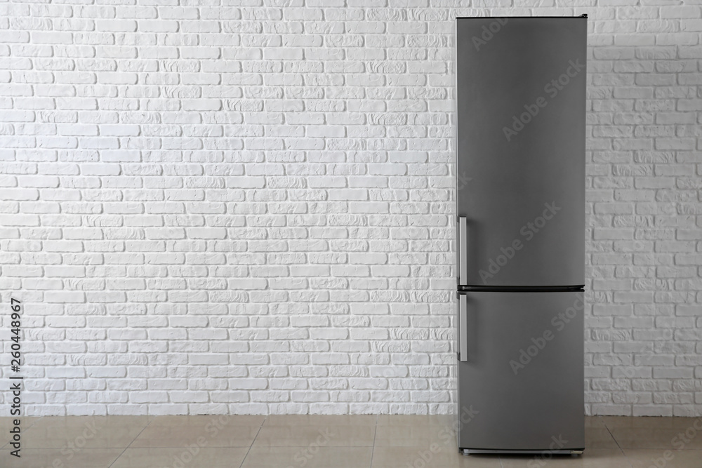 Modern fridge near white brick wall