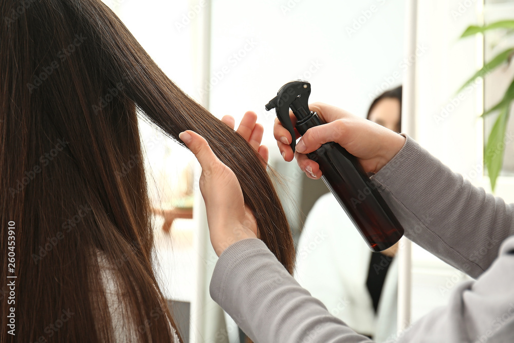 Hairdresser working with long hair of young woman in salon