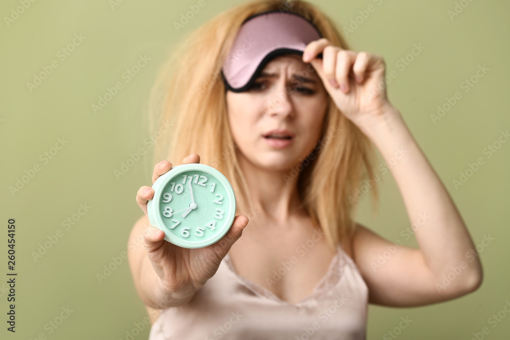 Sleepy woman with mask and clock on color background