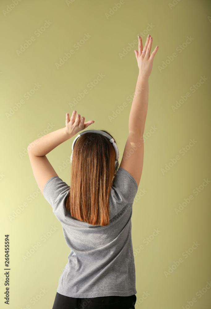 Young woman with headphones listening to music on color background