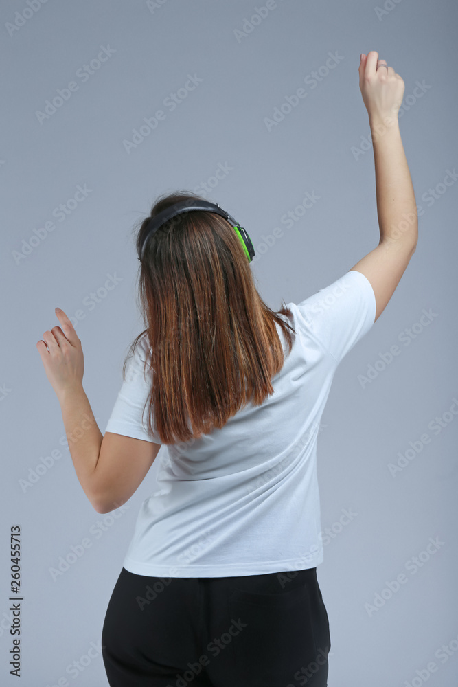 Young woman with headphones listening to music on grey background