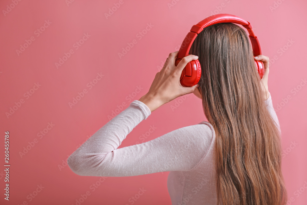 Young woman with headphones listening to music on color background