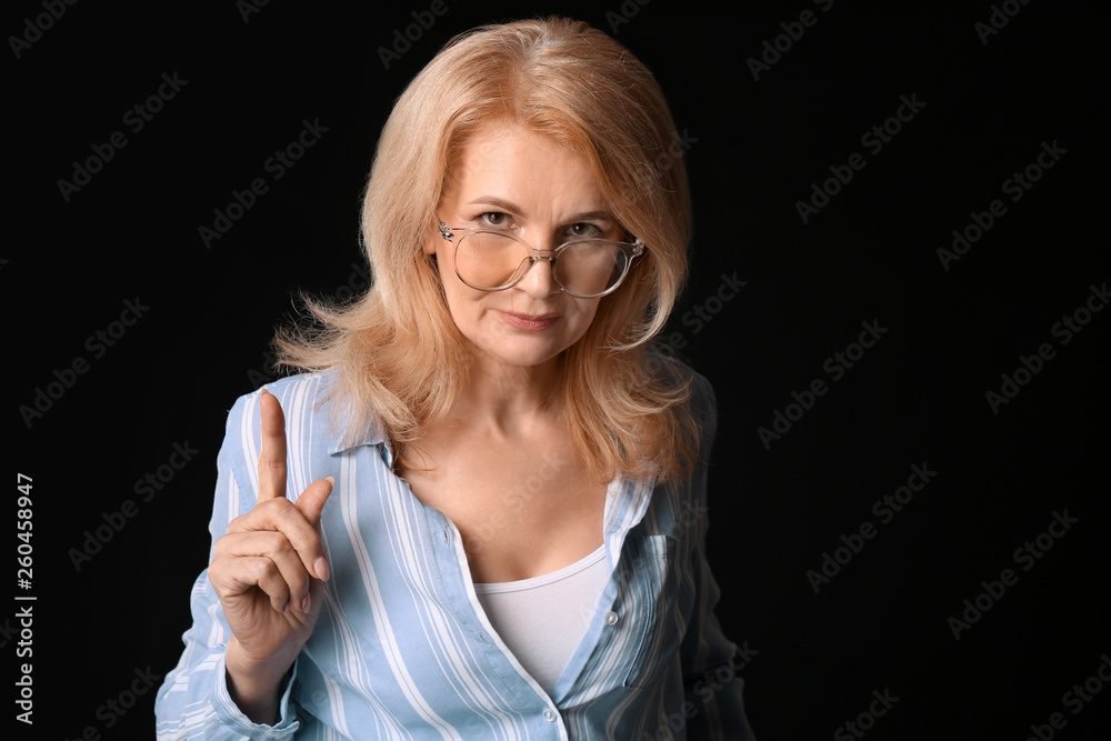 Mature woman with raised index finger on dark background