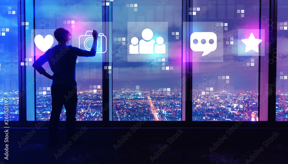 Social media with man writing on large windows high above a sprawling city at night