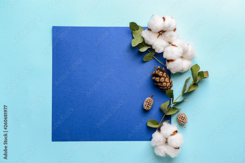 Cotton flowers with sheet of paper on color background