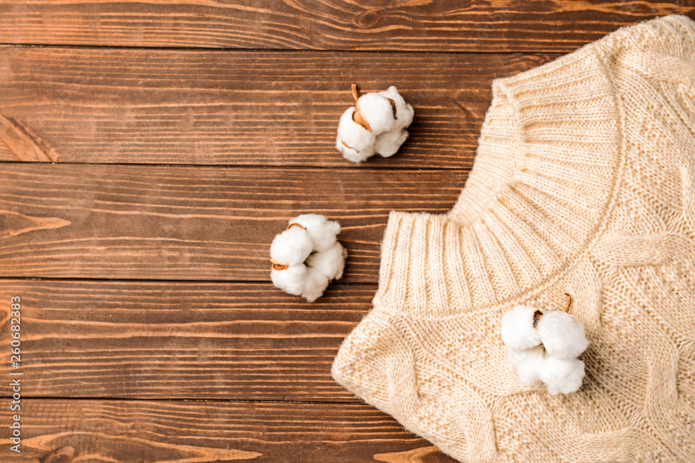 Cotton flowers with knitted sweater on wooden background