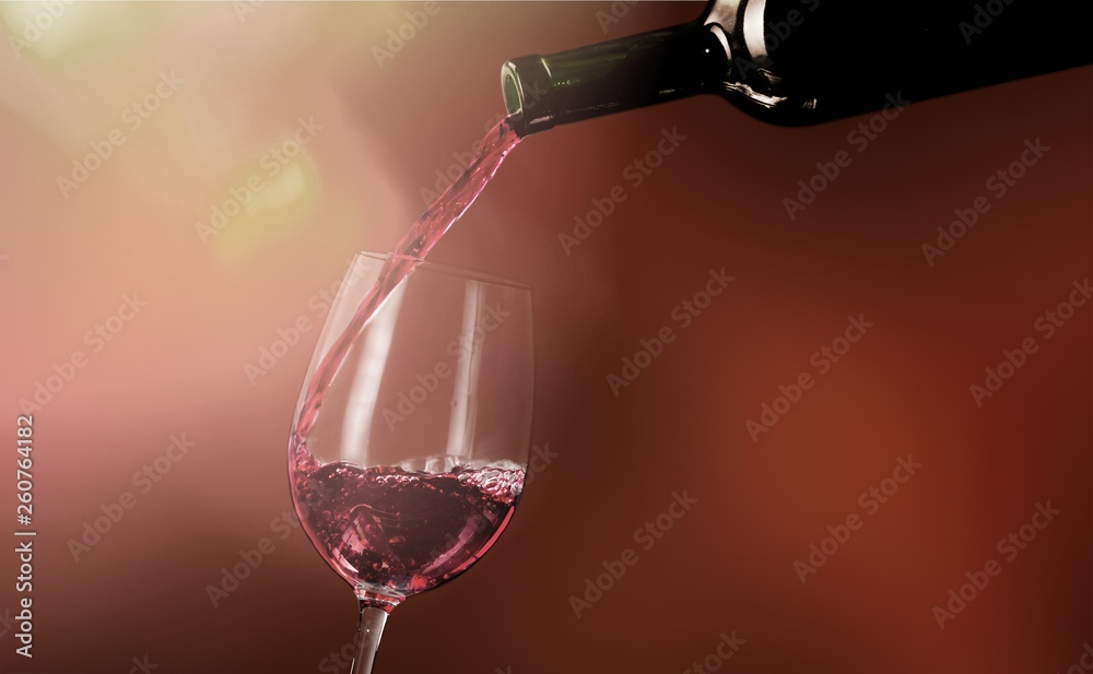 Red wine pouring into glass on background