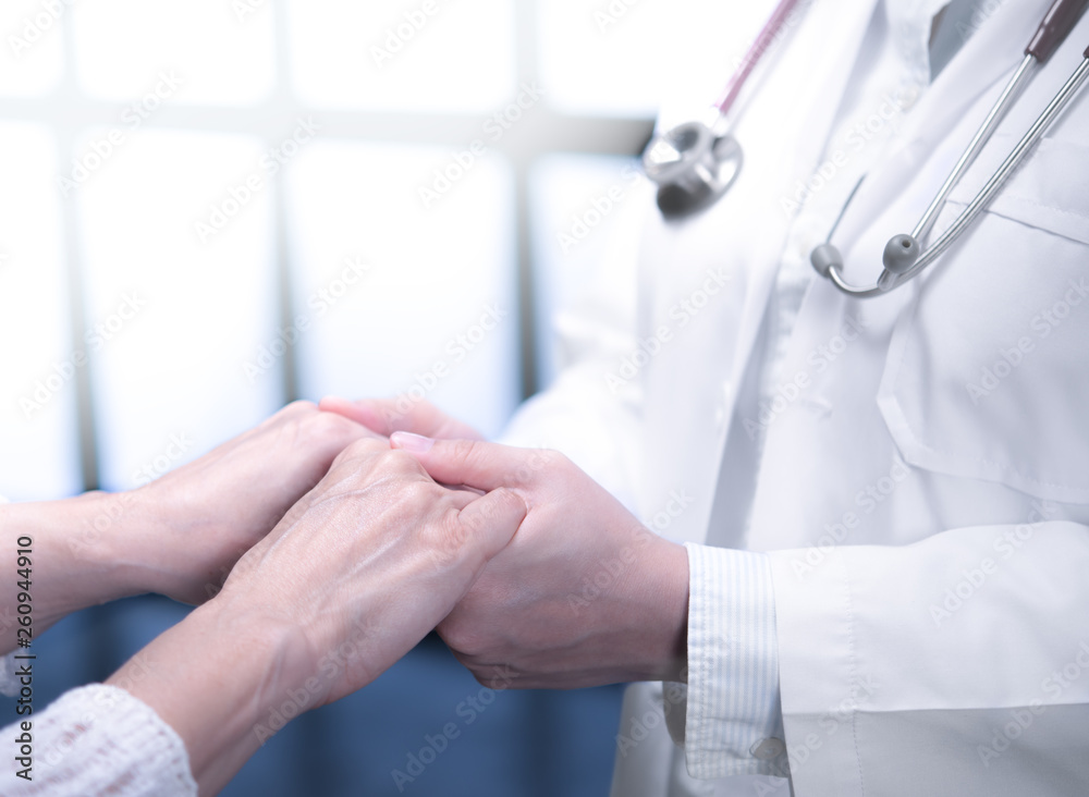 Medical doctor reassuring patient by holding patient’s hands in hospital setting