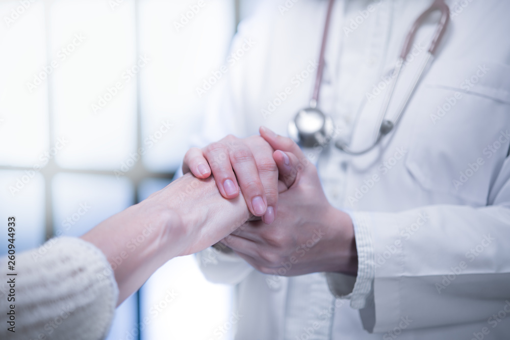 Medical doctor reassuring patient by holding patient’s hands in hospital setting