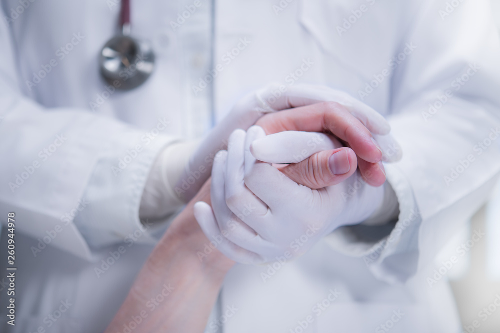 Medical doctor wearing latex gloves holding patient’s hand to give support in hospital setting