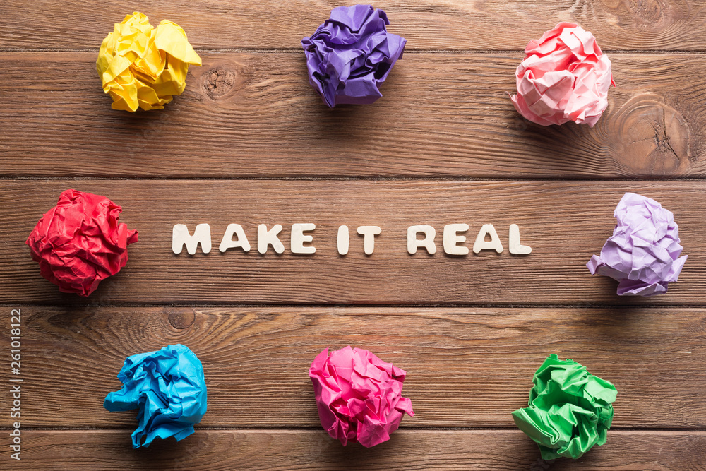 Make it real phrase on wooden table and paperballs around