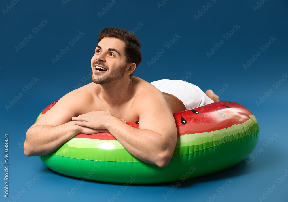 Handsome man relaxing on inflatable ring against on color background