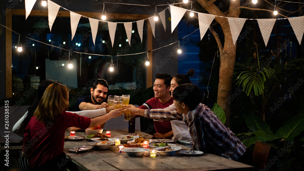 Asian group eating and drinking cold beer outside the house at night, having fun talking