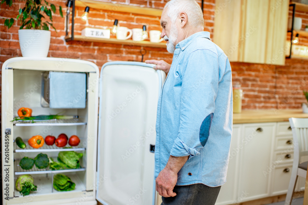 Senior man opening refrigerator full of healthy fresh products on the kitchen at home