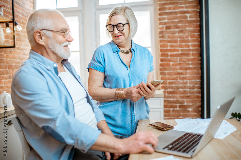 Beautiful senior couple in blue shirts sitting together with laptop on the kitchen at home