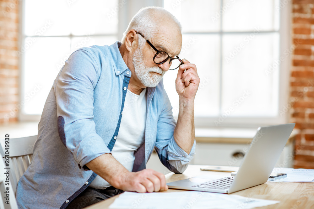 Handsome senior man dressed in blue shirt working with laptop at home