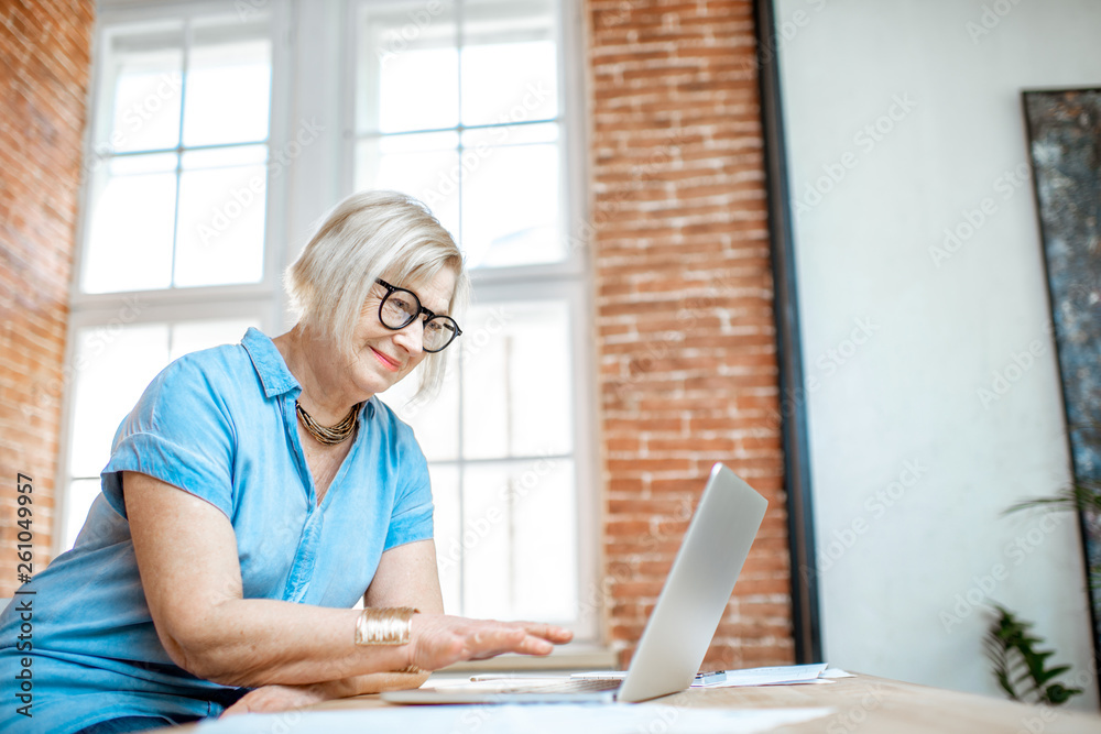 Beautiful senior woman working with documetns and laptop on the kitchen at home