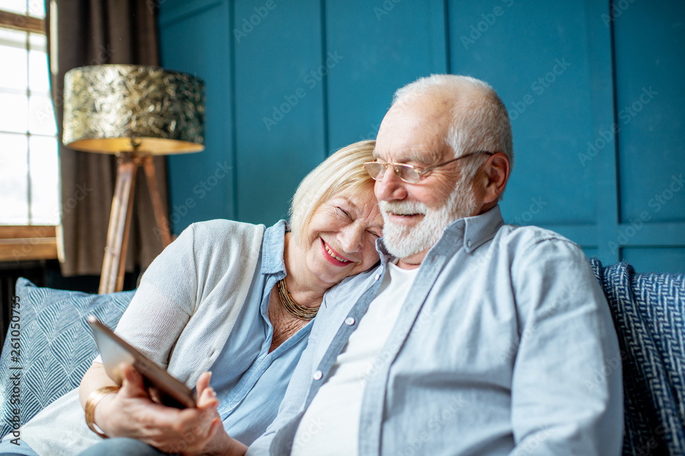 Lovely senior couple dressed casually using digital tablet while sitting together on the comfortable