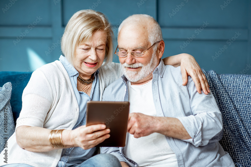 Lovely senior couple dressed casually using digital tablet while sitting together on the comfortable