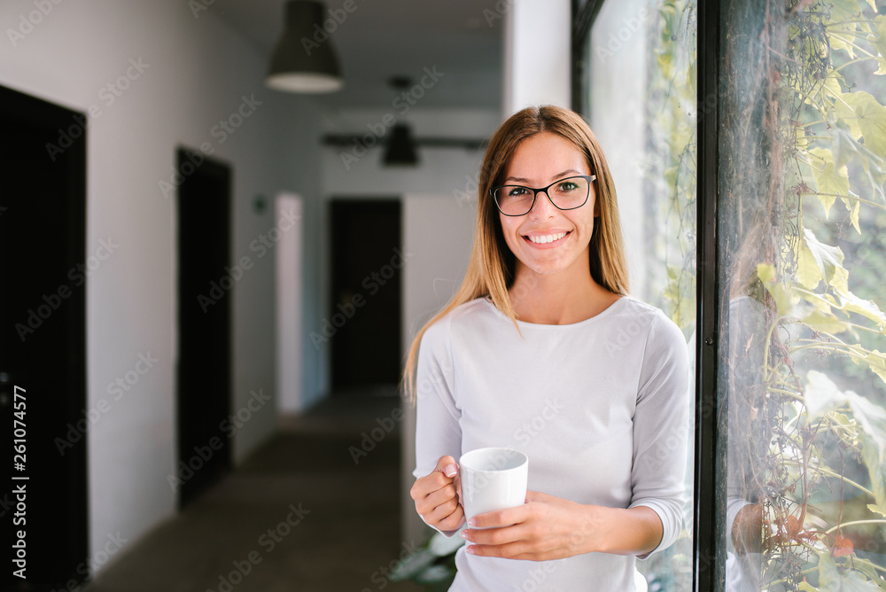 室内拿着马克杯微笑的年轻女子的肖像。