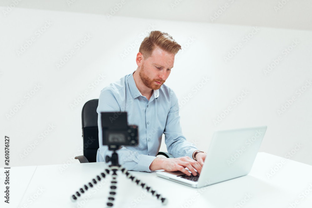 Ginger millenial vlogger using laptop in bright office.