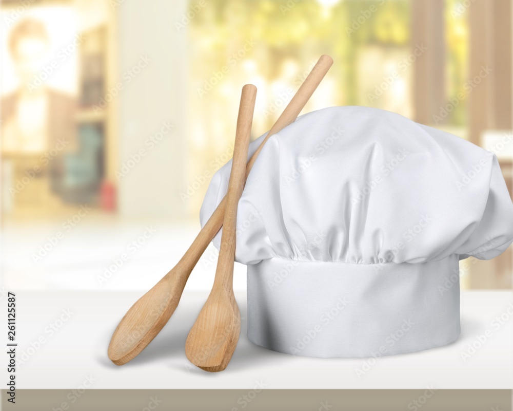 White cooks cap and wooden spoons on wooden table