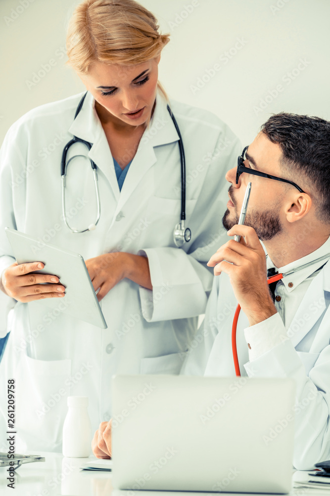 Doctor at hospital office working on laptop computer on the table with another doctor having discuss