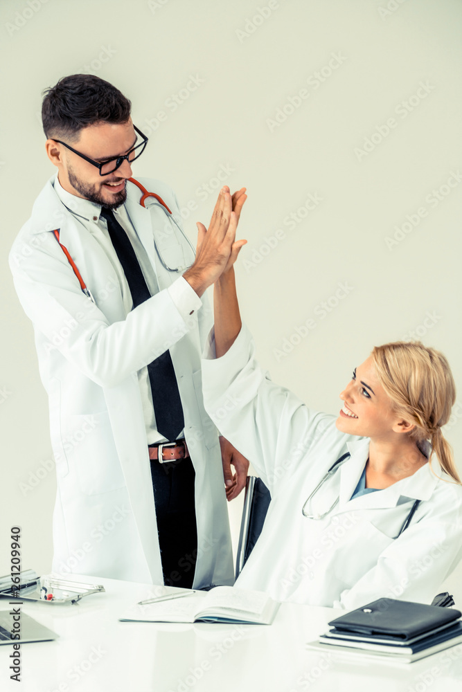 Happy successful doctor celebrates victory in hospital office with another doctor standing beside he