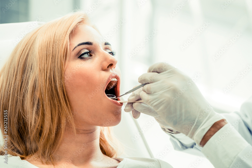 Young handsome dentist examining teeth of happy woman patient sitting on dentist chair in dental cli