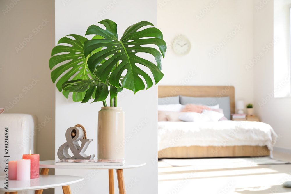 Vase with tropical leaves on table in room