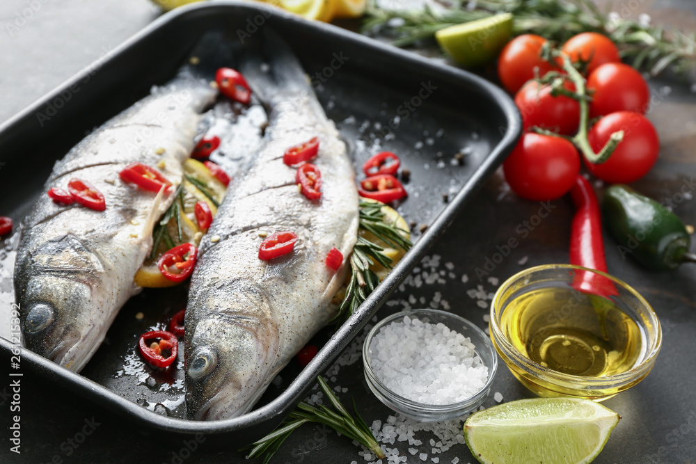 Baking tray with fresh fish and ingredients on dark table