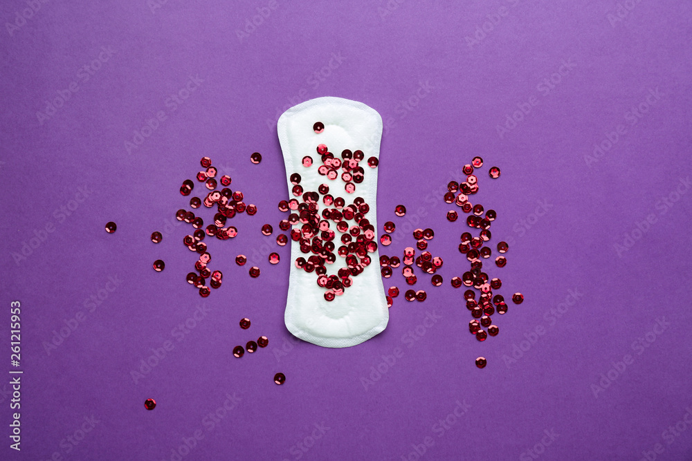 Menstrual pad with red sequins on color background. Menstruation concept