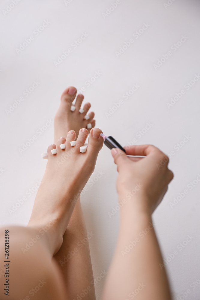 Woman doing pedicure on light background