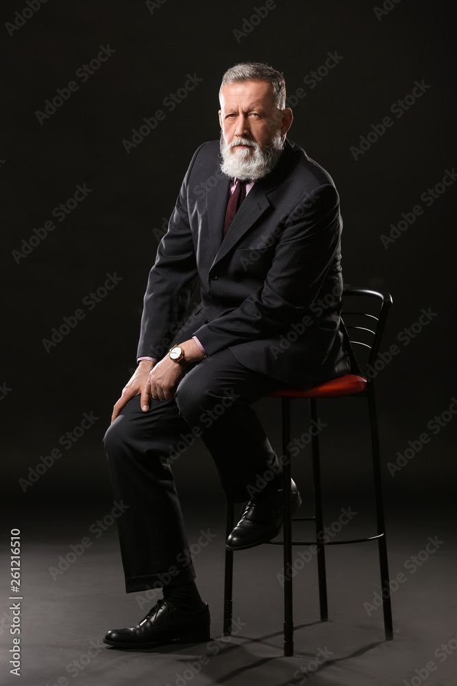 Handsome mature businessman sitting on chair against dark background