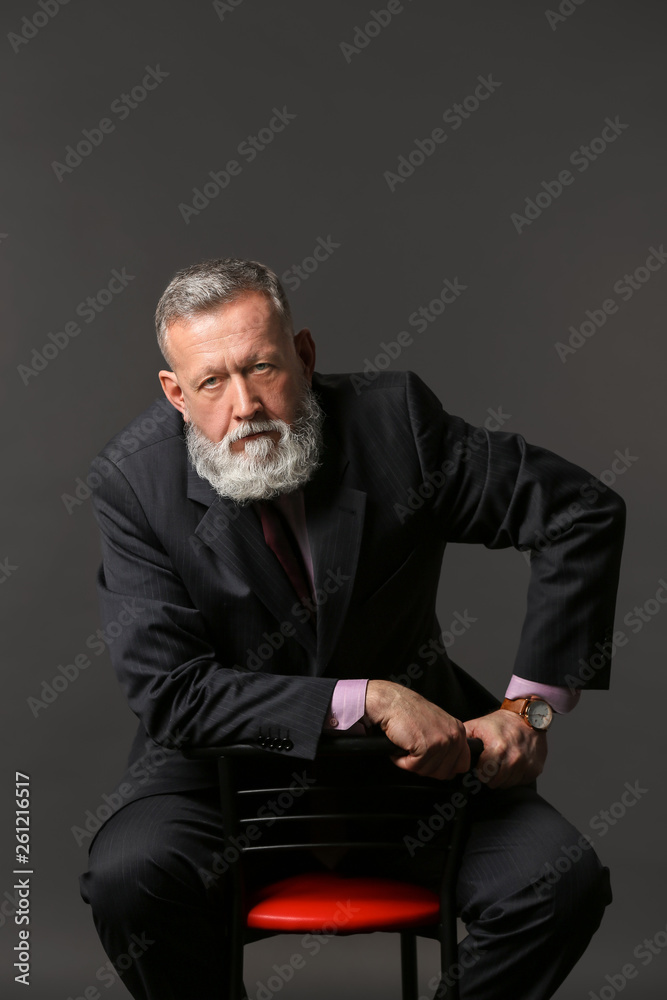 Handsome mature businessman sitting on chair against dark background