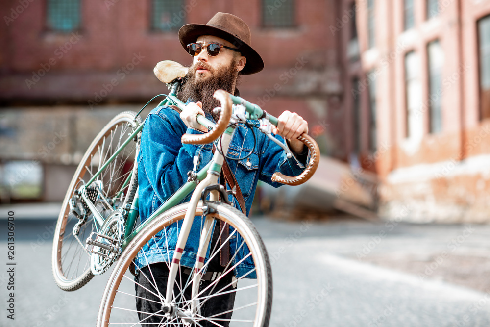 Lifestyle portrait of a bearded hipster dressed stylishly with hat and jacket carrying his retro bic