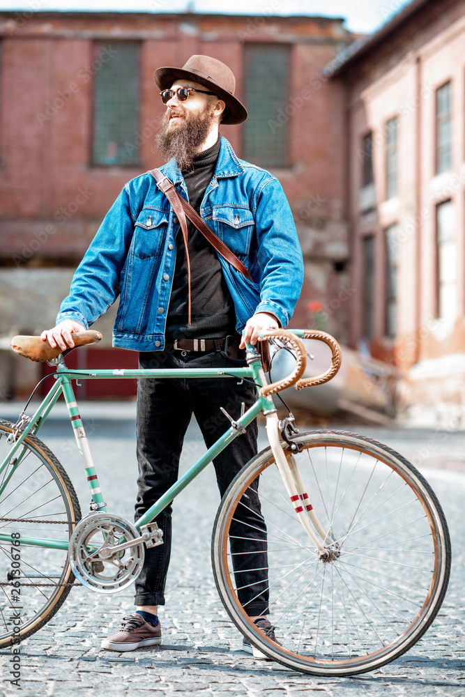 Lifestyle portrait of a bearded hipster dressed stylishly with hat and jacket standing with retro bi