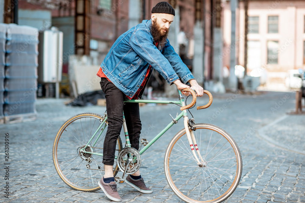 Lifestyle portrait of a bearded hipster dressed stylishly with hat and jacket standing with retro bi