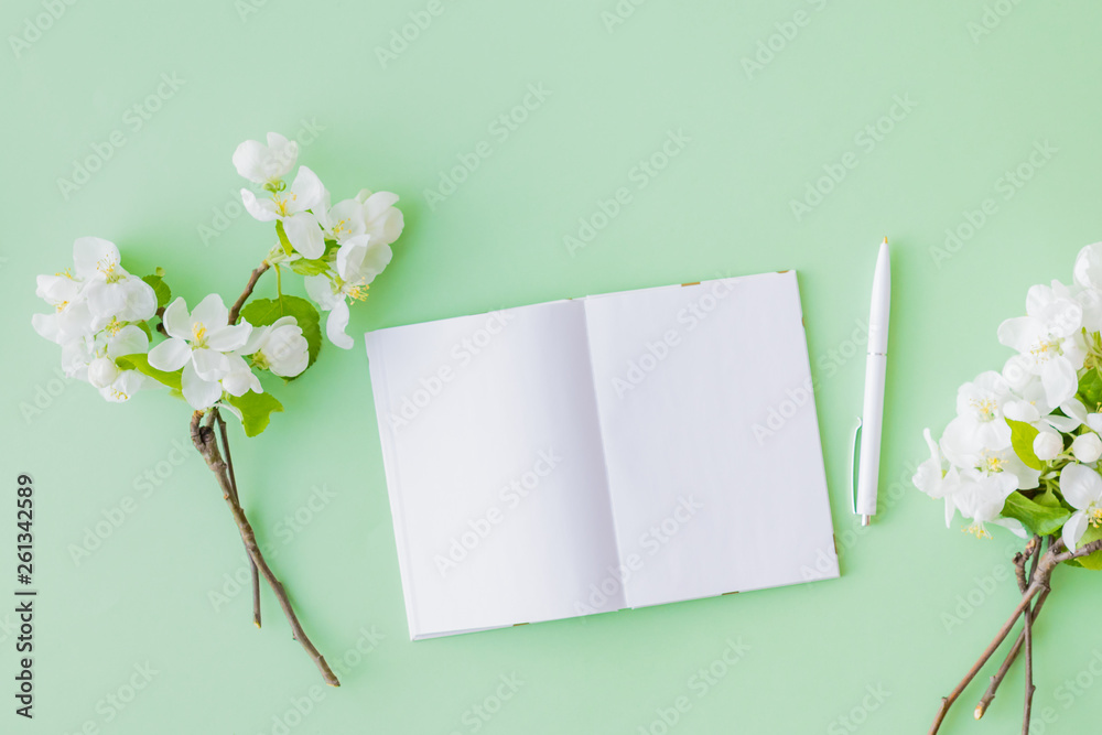 Mockup white open notebook with spring white flowers on a green background