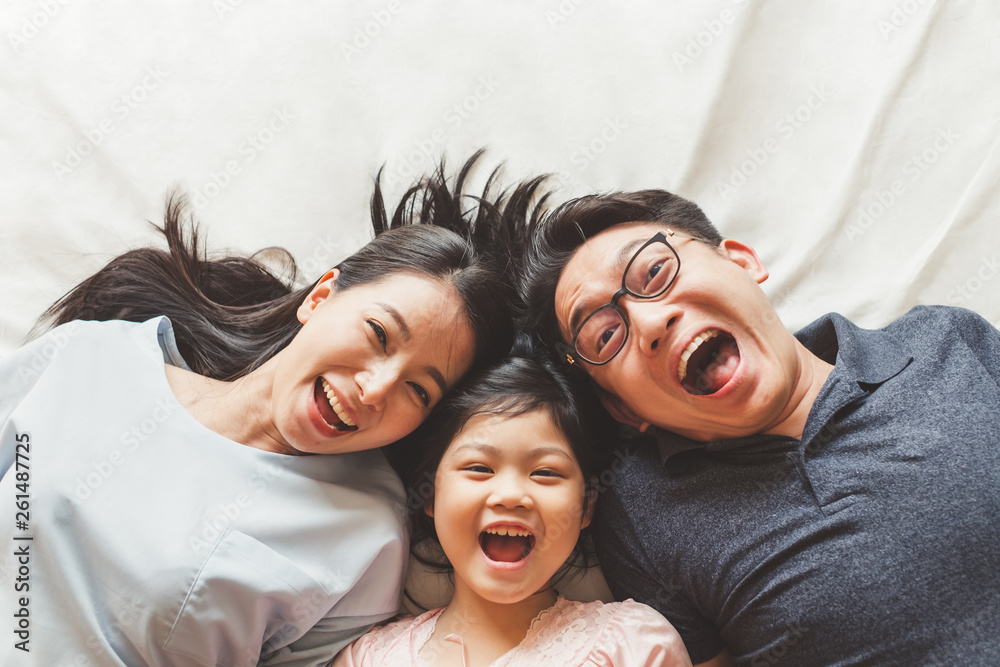 Happy Asian family laying on bed in bedroom with happy and smile, top view