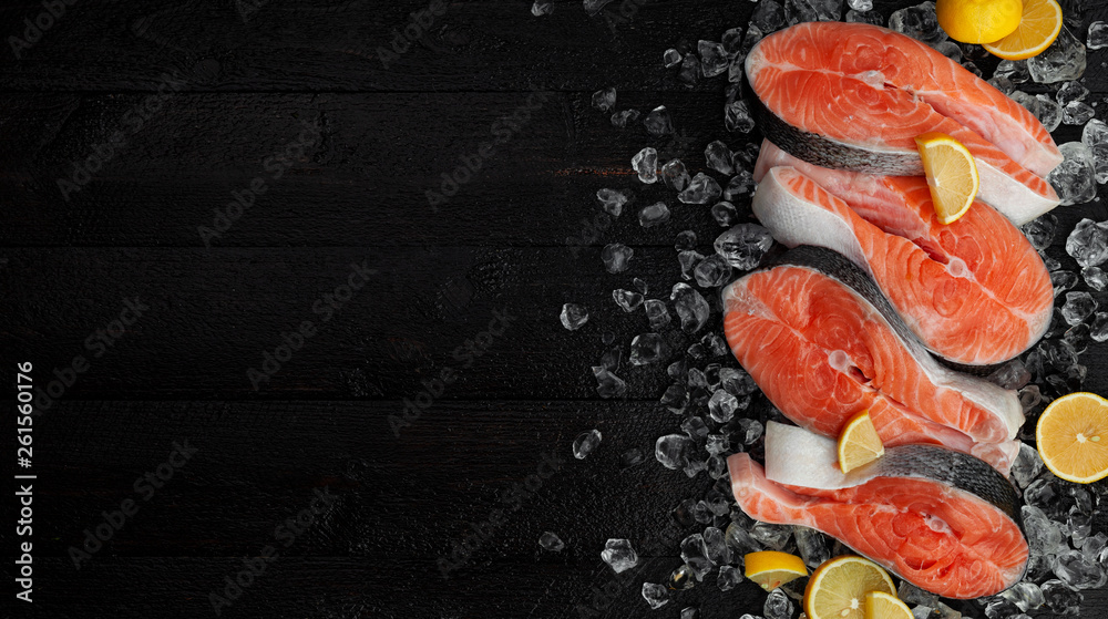 Fresh salmon steaks on black background, piece of chilled red fish on ice, top view