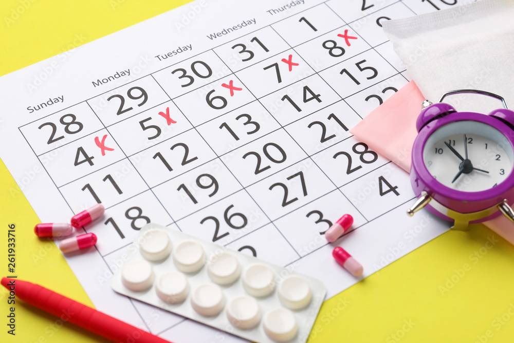 Menstrual calendar with pills and alarm clock on color background