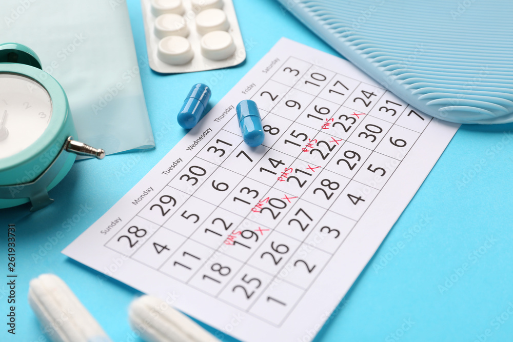 Menstrual calendar with feminine products and pills on color background