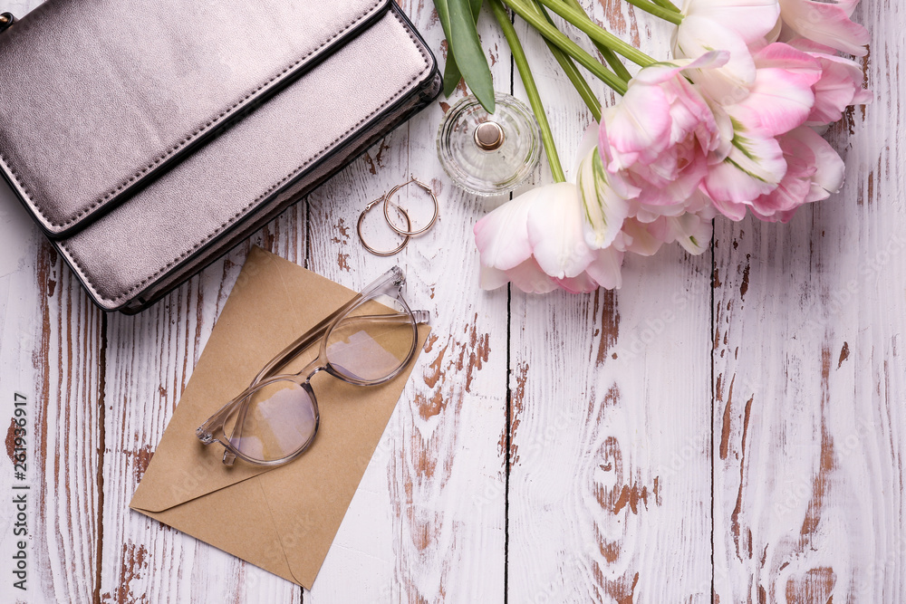 Beautiful tulips with envelope and female accessories on white wooden background