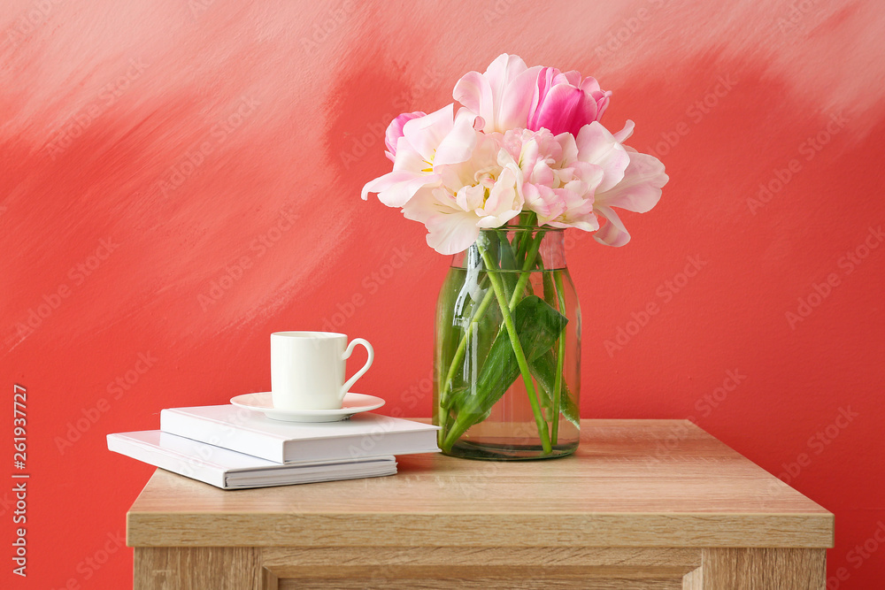 Vase with beautiful tulips, books and cup of coffee on table against color background