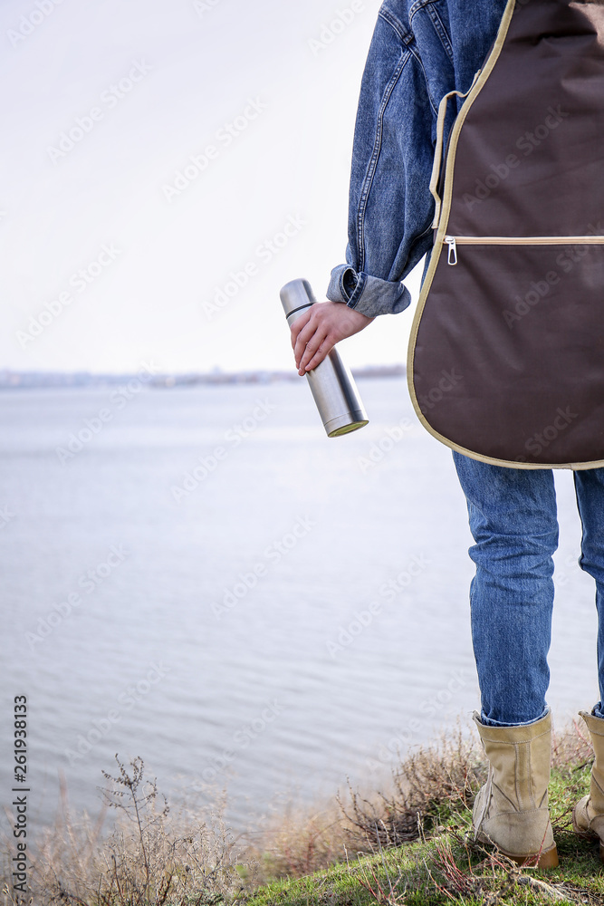 河边拿着保温瓶和吉他的女人，后视图