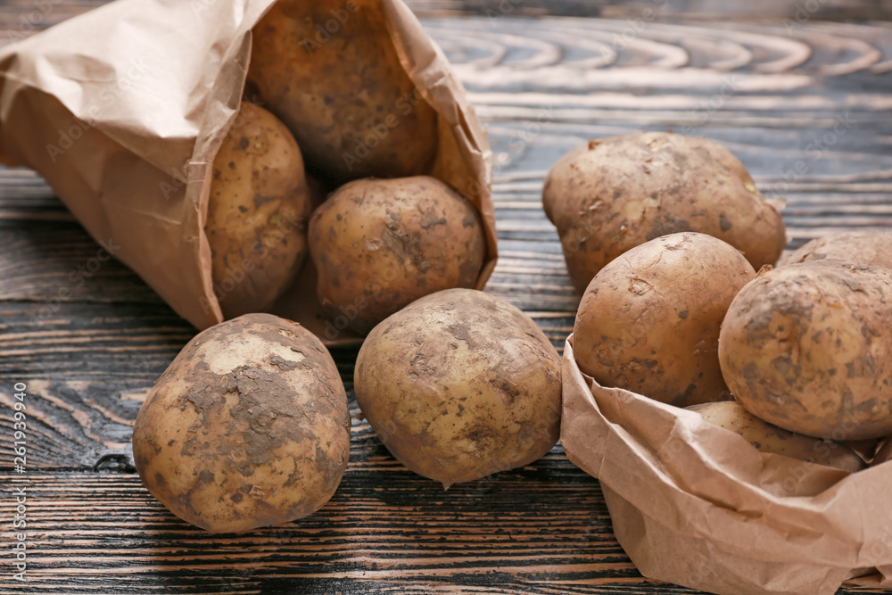 Bag with raw potatoes on wooden table